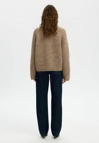 Pull en tricot beige épais avec une coupe décontractée, texture côtelée et manches longues, associé à un jean large bleu foncé.