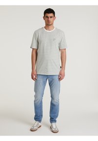 T-shirt a righe a maniche corte in grigio chiaro e bianco, con un piccolo patch del logo verde. Abbinato a jeans azzurri e sneakers casual.