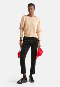 Pull en maille beige avec des poignets côtelés, pantalon en velours côtelé noir, chaussures en cuir verni noir, et accessoires rouges comprenant un chapeau et un sac.