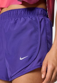Calções atléticos roxos com uma cintura elástica, apresentando um painel lateral texturizado e um pequeno logótipo da Nike em branco no canto inferior esquerdo.