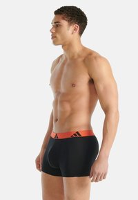 Svarta boxerbriefs med en kontrasterande orange resår i midjan med svarta logotyper. Mjukt tyg och tajt passform, sedd från sidan.