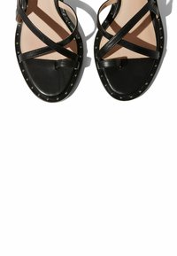 Crne kožne sandale s ukriženim trakama, ravnim potplatom i ukrasnim zakovicama oko ruba. Glatka tekstura na gornjem dijelu.