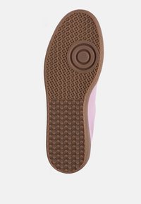 Suola della scarpa in gomma marrone con un motivo di presa testurizzato, caratterizzata da un accento circolare. Il lato mostra un materiale rosa che si estende verso l'alto.