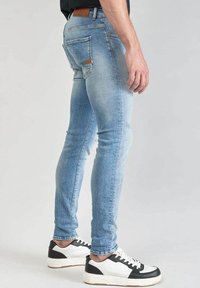 Vaaleansiniset slim fit -farkut, joissa on kulutettu viimeistely, takataskut ja vaalea nahkalaatta. Yhdistetty valkoisiin ja mustiin lenkkareihin.