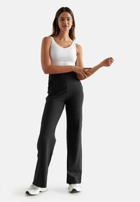 Pantaloni neri a gamba larga con una texture liscia e vita alta, abbinati a una canotta bianca e a scarpe da ginnastica bianche.