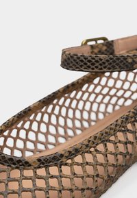 Καφέ επίπεδο παπούτσι με σχέδιο φίδιου δέρματος από δίχτυ, με λουράκι στον αστράγαλο και χρυσή αγκράφα, που δείχνει λεπτομερή υφή και ανοιχτό σχεδιασμό πλέγματος.