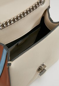 Obdélníková kabelka z béžové kůže se stříbrným řetízkovým popruhem, s barevnou akcentní panelem a magnetickým zapínáním. Viditelné vnitřní přihrádky.