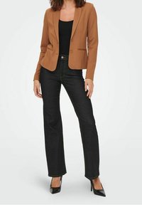 Blazer marron sur mesure avec un seul bouton, associé à un jean noir évasé et des talons hauts noirs. Design minimaliste avec une texture lisse.