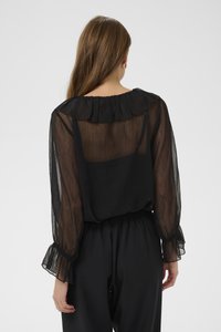 Blusa nera trasparente con scollo arricciato, maniche lunghe a sbuffo e tessuto strutturato. Abbinata a pantaloni neri con vita elastica.