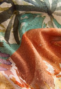 Pehmea tekstuuriga kangas, millel on abstraktsed lillemustrid oranžides, türkiissinistes, lillades ja beežides toonides ning õrnad voldid.