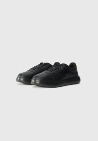 Las zapatillas negras cuentan con un upper de cuero liso, cierre de cordones tradicional, suela acolchada y un discreto logo en el costado.