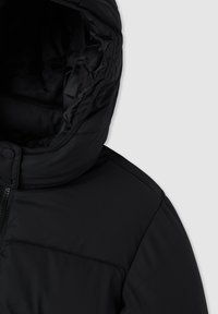 Czarna kurtka puchowa z wysokim pikowanym kołnierzem, zapięcie na zatrzaski i widoczny zamek błyskawiczny na jasnoszarym tle.