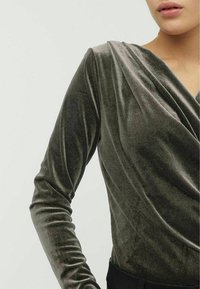 Haut en velours vert à manches longues avec un col drapé, une texture lisse et une coupe ajustée. Présente une finition subtilement brillante.