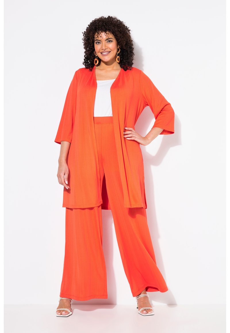 Set leggero e brillante arancione composto da due pezzi, con pantaloni a gamba larga e una giacca lunga in stile kimono aperta davanti sopra a una maglietta bianca.
