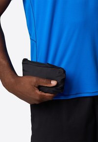 Black zippered pouch held in a hand, featuring a smooth texture. Worn with a blue textured athletic shirt and black shorts.