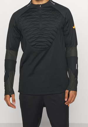 Zwarte sporttop met lange mouwen, gewatteerd ontwerp bij de borst, duimgaten in de mouwen, halve ritssluiting aan de voorkant en kleine oranje Nike-logo's op de rechtermouw en broek.
