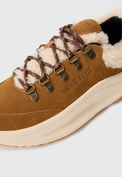 Brune ruskinds sneakers med cremet pelsforing, mønstrede brune snørebånd, metaløjer og "MOON BOOT" prægede på siden.