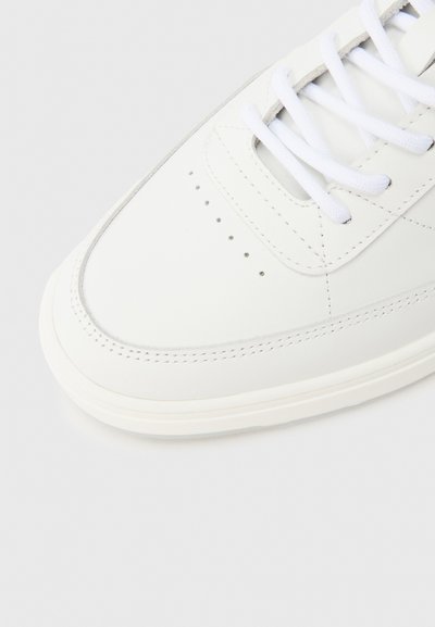 Fehér bőrből készült sportcipő sima felülettel, kerek orral és perforációs részletekkel. Fehér fűzőkkel és finoman dombornyomott logóval díszített.