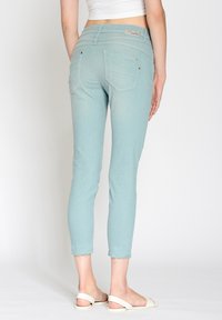 Jasnoniebieskie dżinsy z denimu o dopasowanym kroju, z talią sięgającą środka, tylnymi kieszeniami i postrzępionymi mankietami. Noszone z białymi sandałami.