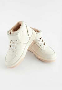 Baskets montantes blanches en cuir lisse avec un devant à lacets et une sangle velcro. Dotées d'une doublure beige douce et d'une semelle en caoutchouc.
