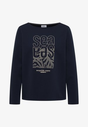 Marineblauw shirt met lange mouwen en een ronde hals, met beige gestippelde tekst "sea eas" en "seaside ease moments" en patronen van golven en bladeren.