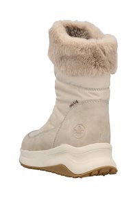 Bota de invierno beige con puño de pelo sintético, suela gruesa y logo bordado en el costado, en ángulo para mostrar la parte trasera y lateral.