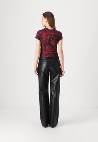 Black leather wide-leg pants paired with a fitted red graphic t-shirt featuring intricate black patterns and short sleeves.