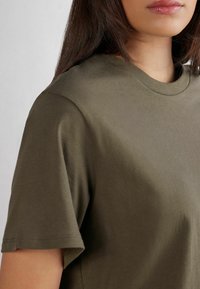 Olivgrön T-shirt gjord av ett mjukt, slätt tyg. Kort ärm med en klassisk rund nacke. Inga synliga mönster eller hårdvarudetaljer.