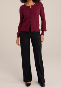 Vínový kardigan s žebrovanou strukturou a zapínáním na knoflíky, kombinovaný s černými kalhotami s prou�žky a černými balerínami. Dlouhé rukávy s nařasenými detaily.