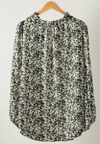 Blomstret bluse med mørk baggrund og elfenbensfarvede blomster, lange ærmer, en samling rundt om halsen og en afrundet kant. Fremstillet af letvægtsstof.