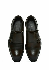 Ruskeat nahkakengät, joissa on teksturoitu pinta, kaksi metallista solkea ja pyöreä kärkimalli. Tyylikkään sulava kokonaisilme.