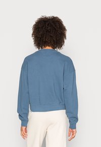 Sudadera azul corta con mangas largas, cuello redondo y dobladillo acanalado. Textura suave, ajuste informal, diseño sin adornos.