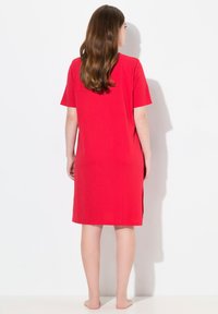 Robe t-shirt en coton rouge avec des manches courtes, coupe au genou et fentes sur les côtés. Texture lisse avec une coupe décontractée.