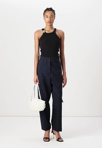 Top en maille noir à fines côtes, pantalon taille haute bleu marine, sandales à talons noires et un sac à main blanc au design doux et arrondi.