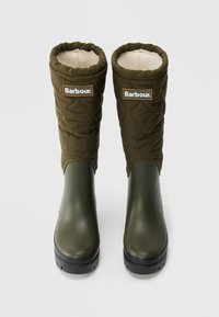 Een paar groene Barbour geïsoleerde rubberlaarzen met een bovenkant van gewatteerde stof en een fleecevoering, gezien van voren op een witte achtergrond.