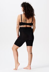 Sorte shapewear shorts går til midt på låret og har en høj talje. Stoffet ser glat og strækbart ud, designet til komfort og støtte.