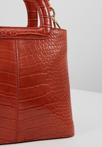 Sac à main en cuir marron avec texture crocodile et anses structurées sur un fond clair.