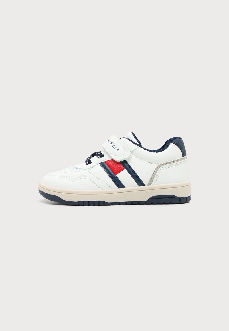 Λευκό sneaker χαμηλού κολακευτικού ύφους με ναυτικό και κόκκινο ρίγες, ναυτικά κορδόνια και λουράκι με βέλκρο με την επιγραφή "Tommy Hilfiger,", εμφανίζεται σε ουδέτερο φόντο.