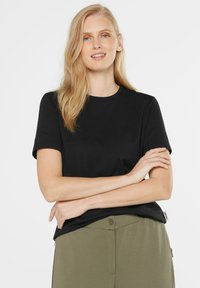 Schwarzes Kurzarm-T-Shirt aus Baumwolle mit Rundhalsausschnitt und lockerer Passform, kombiniert mit olivgrünen Hosen.