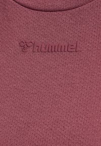 Tummanpunainen teksturoitu kangas, jossa on hienovarainen poimutus ja kohotettu "hummel"-logo samansävyisenä.