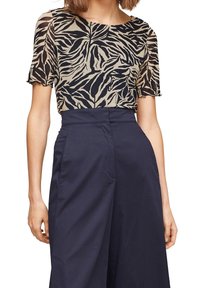 Top de manga corta negro y beige con estampado de cebra, combinado con pantalones de tiro alto en navy. Textura suave, corte relajado y un brillo sutil.