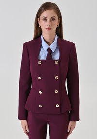 Bordeaux dubbelzijdig colbert met gouden knopen, slim-fit design en vierkante halslijn, gecombineerd met een lichtblauw shirt en stropdas.
