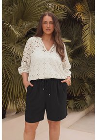 Blusa de crema suave con recortes florales, combinada con pantalones cortos negros con cordón. Ambas prendas tienen siluetas relajadas y texturas suaves.