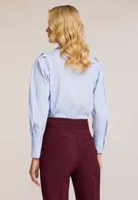 Hellbluse mit Streifen und blusigen Ärmeln sowie geknöpften Manschetten, kombiniert mit hoch taillierten kastanienbraunen Hosen mit Gesäßtaschen.