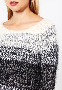 Strickpullover mit einer flauschigen Textur und einem schwarz-weiß-grauen Streifenmuster; weiter Halsausschnitt; weiches, lässiges Design.