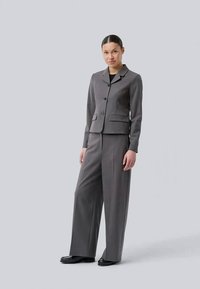 Gray tailored suit consisting of a fitted jacket with a collar and wide-leg trousers, made of smooth fabric, complemented by black shoes.