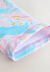 Posnetek blazine na blagu s pastelno modrim, rožnatim in zlatim abstraktnim vzorcem ter rožnatim zaključnim šivom na belem ozadju.