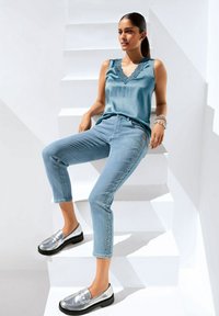 Hellblaues Satintanktop mit Spitzenbesatz, kombiniert mit hellblauen Jeans mit Strassdetails. Silberne Slipper mit schwarzen Sohlen.