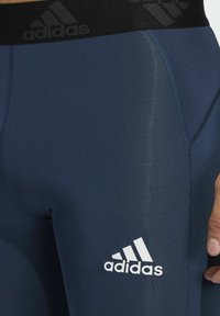 Knee-żeglarskie legginsy w kolorze granatowym, wykonane z elastycznego materiału. Posiadają czarny pas z logo marki Adidas oraz białe oznaczenie na dolnej części nogawki.