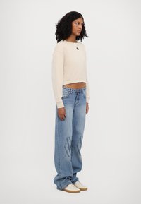 Sweatshirt beige cropped con scollatura rotonda e orlo a coste abbinato a jeans azzurri a gamba larga con stampa del logo sulla coscia.